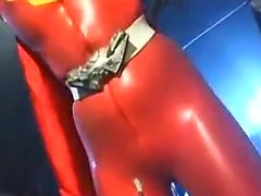 Sexy Super Hero in orange latex is strung up and tortured b